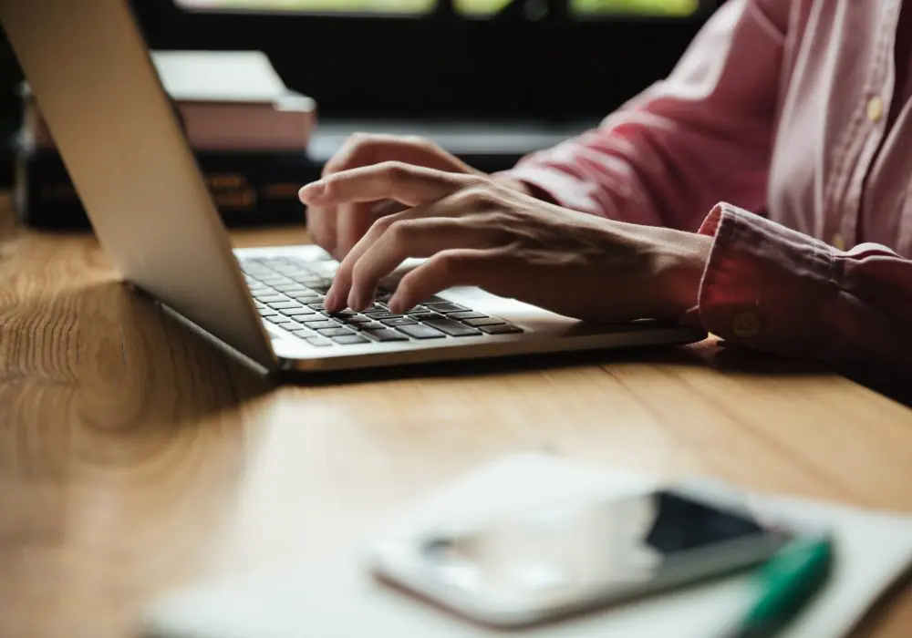 Cropped side view of woman sitting by the table in cafe and using laptop computer